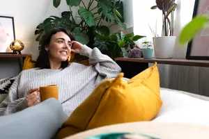 A woman sitting on a couch with a mug in her hand and a smiling face