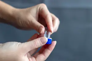 A person holding a blue-colored plastic piece in their hands, probably a medicine bottle