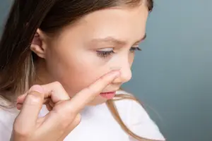 A young girl in a white shirt attempts to put a contact lens in her eye