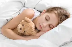A little girl is sleeping on a bed while holding a teddy bear.