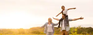 A family of three standing in a field with their arms outstretched