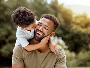 A man with a happy face is carrying a child on his shoulders while smiling and seems to be posing for a photo