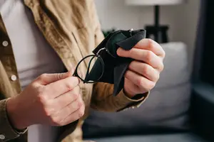 A person is holding a pair of glasses and a black cloth in his hands, probably cleaning the glasses.