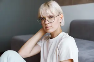 Portrait of a woman with short blonde hair wearing glasses and sitting on a couch.