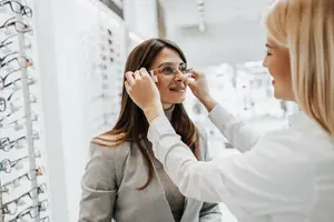 An optician is helping a woman try on a pair of glasses inside of a store