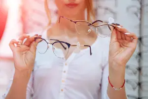 A woman is looking at glasses in front of a glass window