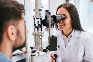 A woman in a white lab coat is using a device to look into a man's eye.