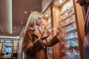 A woman wearing glasses is looking at a display case of eyeglasses in a shop