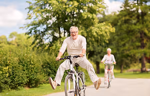 Two elderly people riding bicycles in a park, one of them smiling and jumping in the air