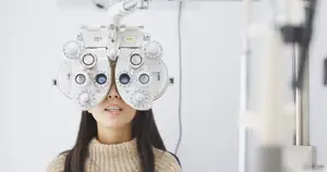 A young woman with long hair is looking through a pair of eyeglasses with a white frame and blue lenses, she is smiling and seems to be in a room with a white wall and a white ceiling.