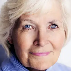 Portrait of an elderly woman with short blonde hair and blue eyes, smiling and looking forward