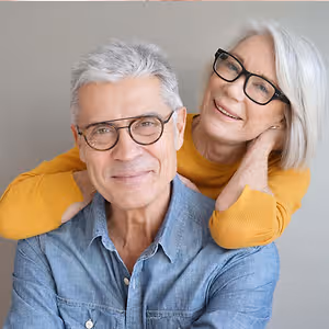 A smiling elderly man and woman are posing for a picture while standing close to each other