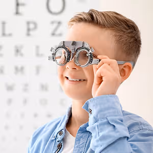 A young boy is holding a pair of glasses with lenses in front of an eye chart.