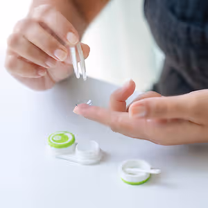 A woman is putting on a contact lens using tweezers.