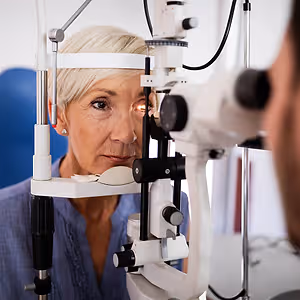 An older woman having an eye exam with a white and black eye machine