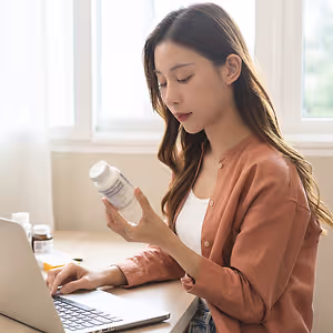 A woman is using a laptop and checking pills in a bottle