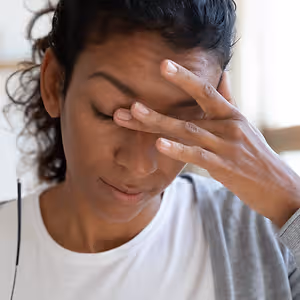 A woman with curly hair and glasses on her left side touching her forehead with her right hand, possibly having a headache
