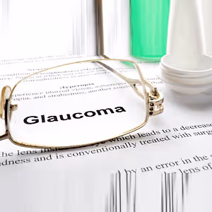 Close up of glasses and a bottle of eye drops on a piece of paper with the word Glaucoma