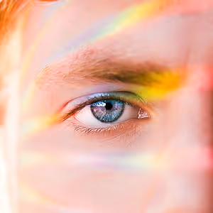A close-up view of a person's eye with a rainbow-like color around it.