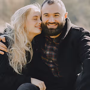 A man and a woman sitting in a park and smiling for the camera