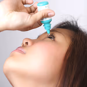 A woman is administering eye drops to her left eye.