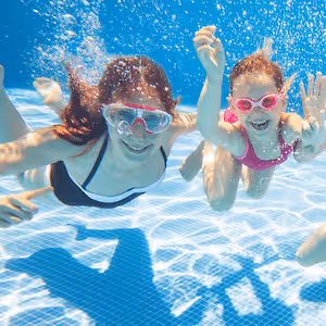 Three children wearing goggles are swimming and playing in a swimming pool.