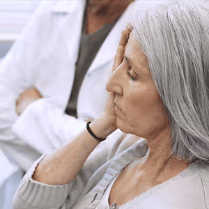 A woman in a white sweater sitting in a medical office looking concerned while touching her face