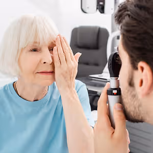 An older woman has her eye examined by a man using a magnifying glass