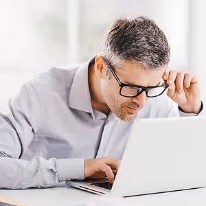 A man adjusting his glasses while using a laptop