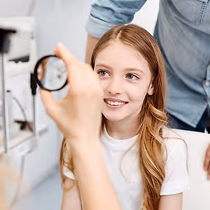 a girl is sitting in a chair and having her eye examined by a doctor