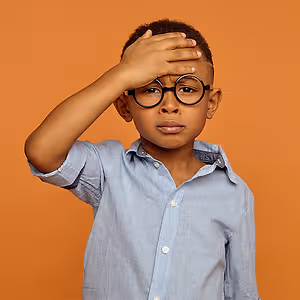 A young boy with glasses covering his eyes with his hand