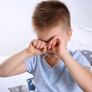 A young boy with brown hair is covering his eyes with his hands, possibly feeling sad or upset.