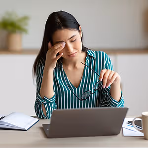 woman sitting at a desk with a laptop rubbing her forehead