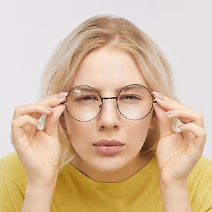 Blonde woman wearing yellow shirt and round glasses adjusting her glasses