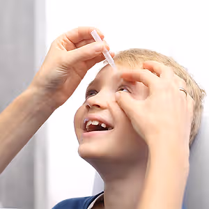A boy getting eye drops administered by a person