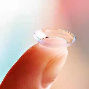 Close-up of a finger holding a transparent contact lens.