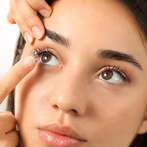 A woman carefully placing a contact lens on her eye, likely in a clinic or medical setting.