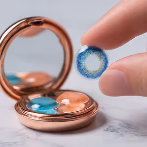A person is holding a blue and white contact lens in their hand in front of a mirror.