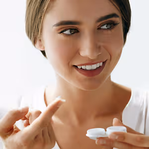 A woman holding a contact lens and looking at it closely