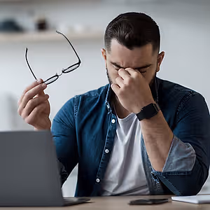 Man with blurry vision adjusting his glasses while working on a laptop