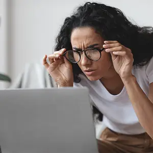 woman adjusting her glasses while looking at a laptop