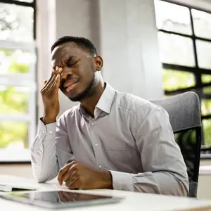 A man sitting at a desk rubbing his eyes with his hand
