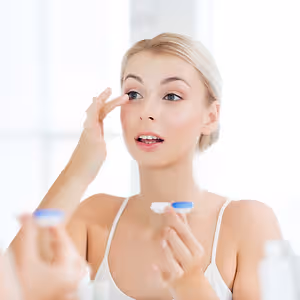 A woman is adjusting her contact lens in front of a mirror