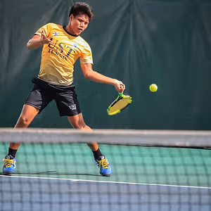 A man in a yellow shirt with UST written on it is playing tennis on a court.