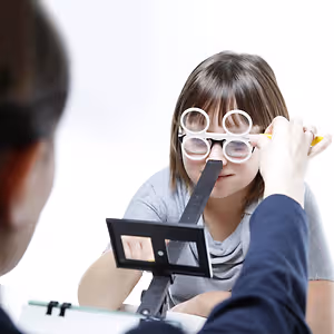 A girl is having her vision tested by an optometrist wearing glasses and holding a pencil.