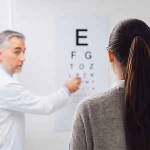 An eye doctor is showing a female patient the eye chart while she looks at it.