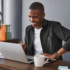 Man sitting at a desk with a laptop and coffee cup smiling