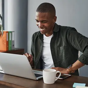 Man sitting at a desk with a laptop and coffee cup smiling