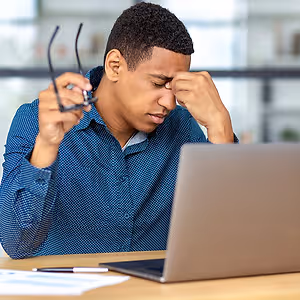 A stressed man with his head in his hands in front of a laptop.