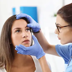 A woman getting her eyebrows waxed by another woman wearing blue gloves.